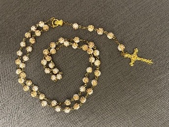 Gold and white rosary beads arranged in a loop on a gray fabric background, with a small gold cross.