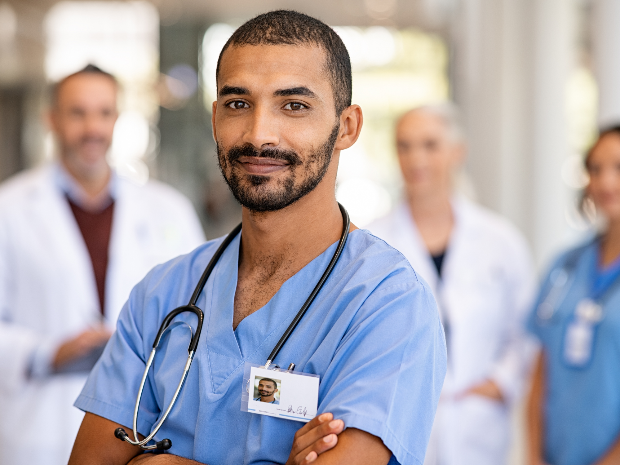 Male doctor in focus with three other doctors in background within hospital setting