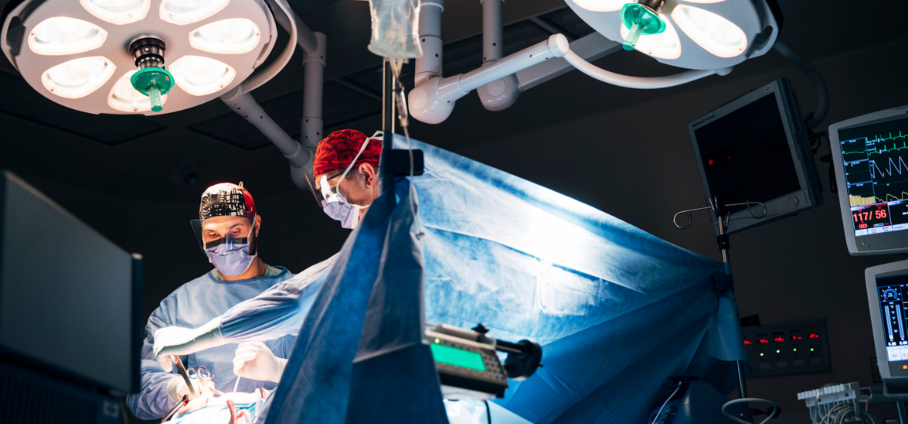 Two surgeons working over a brightly lit operating room table.