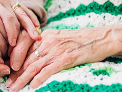 Systemic therapy session, therapist joining palms gently with patient’s hands who lies on bed