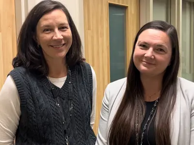 Christine Black and Shannon Bourke dressed in business casual attire, standing together and smiling in a hallway.